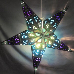 May include: A five-pointed star-shaped paper lantern with a peacock feather design. The lantern features a dark background with teal, purple, and white accents. The star is illuminated, creating a decorative lighting effect.