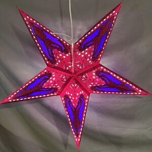 May include: A five-pointed star-shaped hanging lamp featuring a vibrant pink base color with deep purple dolphin silhouettes. The design includes small white circular cutouts along the edges and across the surface, creating a perforated pattern.