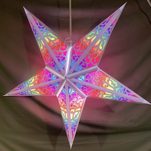 May include: A white paper star lantern with a rainbow iridescent design. The star is hanging from a white string.