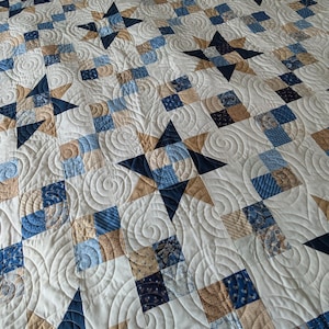May include: A patchwork quilt featuring a repeating pattern of dark blue and tan stars interspersed with squares of various blue and tan patterned fabrics. The entire surface is covered in a continuous spiral machine quilting stitch design.