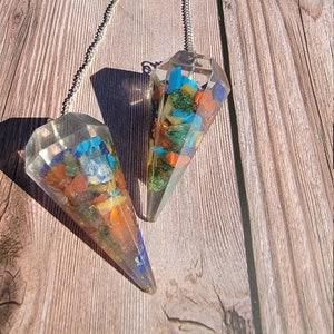 May include: Two clear crystal point pendulums with a silver chain. The pendulums are filled with small, colorful stones, including red, orange, yellow, green, blue, and purple.