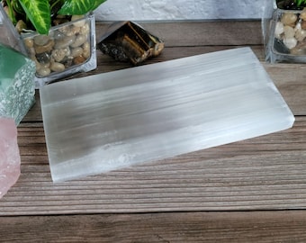 Puede incluir: Una placa de carga de selenita blanca, un tipo de cristal utilizado para la curación energética y la meditación. La placa es lisa y tiene una textura natural estriada.