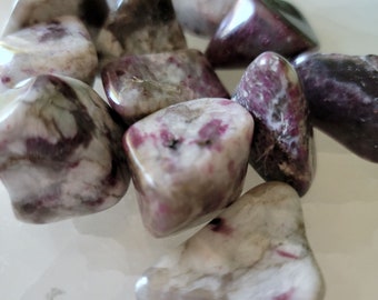 May include: A collection of tumbled pink and white striped stones. The stones are smooth and polished, with a variety of shapes and sizes.