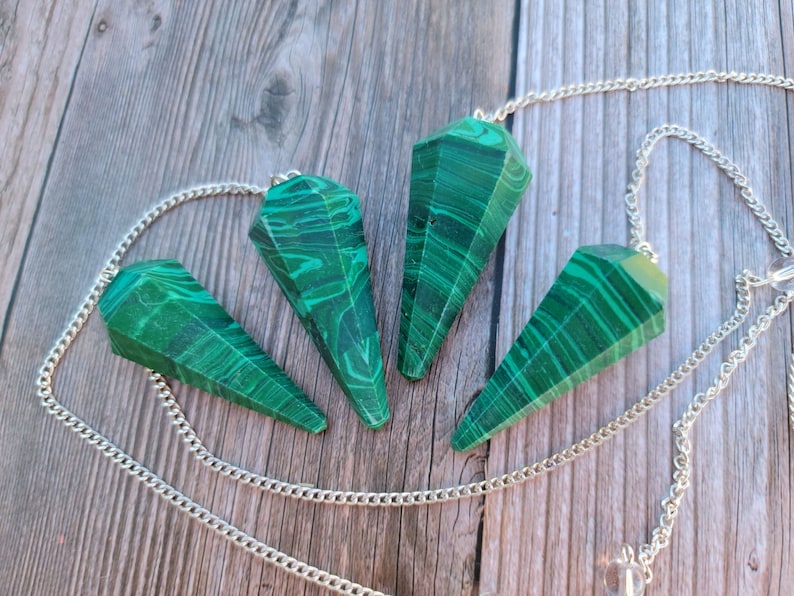 May include: Four green malachite crystal pendulums with silver chains. The pendulums are pointed and have a swirling pattern.