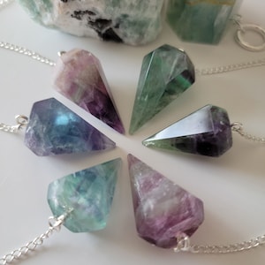 May include: Six fluorite crystal pendulums with silver chains. The pendulums are various shades of green, purple, and blue.