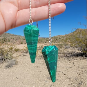 May include: Two green malachite crystal pendulums on silver chains. The pendulums are pointed and have a swirling pattern.