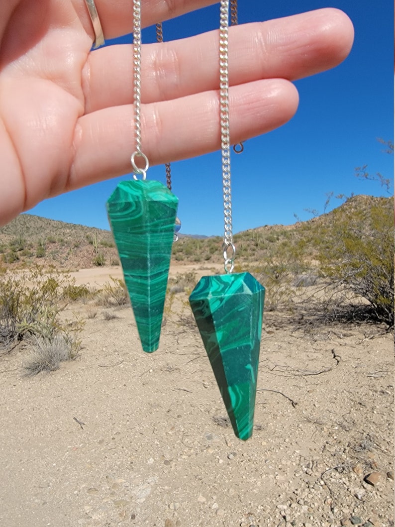 May include: Two green malachite crystal pendulums on silver chains. The pendulums are pointed and have a swirling pattern.