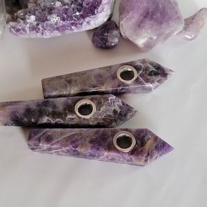 May include: Three amethyst crystal pipes with silver metal bowls. The pipes are different sizes and have a purple and white swirl pattern.