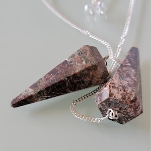 May include: Two brown and white gemstone pendulums on a silver chain. The pendulums are in the shape of a point and are hanging from a silver chain.