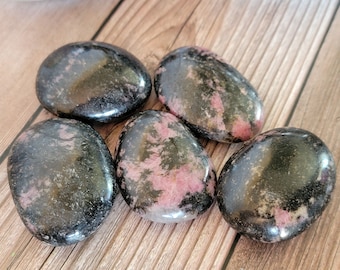 May include: Five smooth, polished stones with a black and pink marbled pattern. The stones are oval shaped and have a glossy finish.