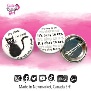 May include: A black and white button with a black cat illustration and the text "It's fine, I'm fine, everything is fine." The back of the button is silver with a safety pin.