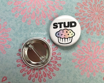 May include: White button featuring a black and white illustration of a cupcake with rainbow sprinkles. The text "STUD" is above the cupcake.