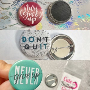 May include: Three 1-inch button pins with motivational quotes. The first pin is red with white text that says "Never Give Up". The second pin is white with black dots and teal text that says "Don't Quit". The third pin is teal with white text that says "Never Give Up".