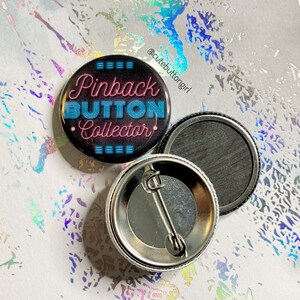 May include: A black button with a neon pink and blue design that says "Pinback Button Collector". The button is shown with its back and a pin back.