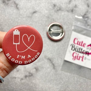 May include: A red button with a white outline of a blood bag, a heart, and the text "I'm a Blood Donor".