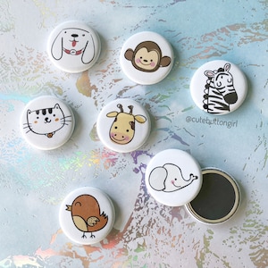 Op de afbeelding: Set van acht witte ronde knoppen met verschillende dierillustraties. De dieren omvatten een hond, een aap, een zebra, een kat, een giraffe, een olifant en een vogel. De knoppen zijn ongeveer 2,5 cm in diameter.