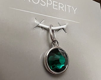 Pode incluir: Um amuleto de prata com uma gema verde escura, apresentado em um cartão branco com a palavra "PROSPERITY" impressa nele.