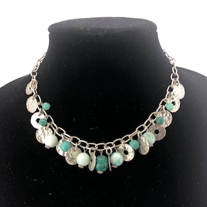 May include: A silver chain necklace with turquoise and silver beads and charms. The necklace has a hammered metal look.