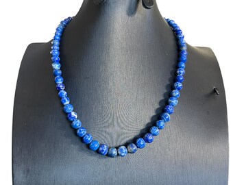May include: A blue lapis lazuli beaded necklace on a black display stand. The necklace is made of round beads with a marbled pattern.