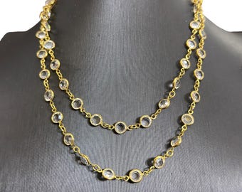 May include: A gold-toned necklace with clear, round gemstones. The necklace is composed of two strands, each featuring bezel-set stones connected by delicate links. The gemstones are evenly spaced along the chain, creating a sparkling effect.