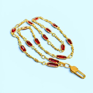 May include: A gold-toned chain necklace featuring a series of elongated, rectangular red glass stones set in metal frames. The chain consists of interconnected oval links and includes a gold-toned lobster claw clasp at one end for secure fastening.