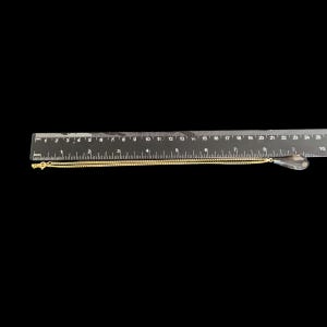 May include: A gold-colored chain necklace with a clear teardrop-shaped pendant. The necklace is laid out on a black surface next to a ruler. The chain is approximately 9 inches long.