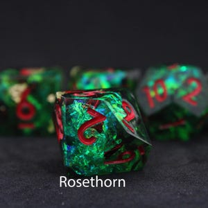 Beautiful green, red and blue resin dice sit on a black felt table top. Light shines down on the dice making the colours swirl into a maelstrom of epic colour. The dice include multicoloured foils that sparkle, shimmer and dance in the light.