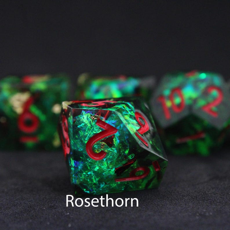 Beautiful green, red and blue resin dice sit on a black felt table top. Light shines down on the dice making the colours swirl into a maelstrom of epic colour. The dice include multicoloured foils that sparkle, shimmer and dance in the light.