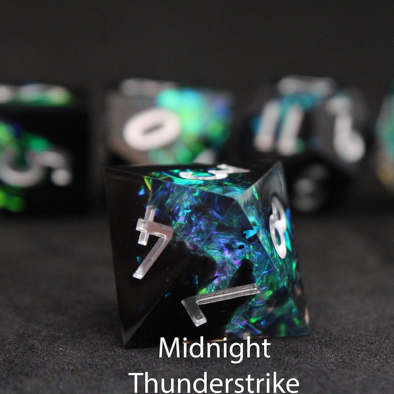 Beautiful black, green and blue edged dice rest on a black felt tabletop. The dice include green and blue foils that shimmer in the light, mimicking a furious lightning storm.