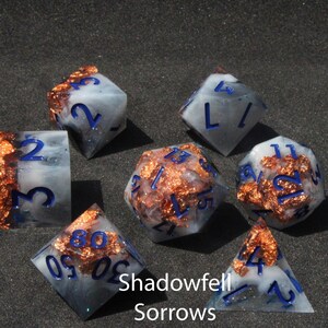 Beautiful blue, black and white resin dice sit on a black felt table top. Light shines down on the dice making the colours swirl into a maelstrom of epic colour. The dice include multicoloured foils that sparkle, shimmer and dance in the light.
