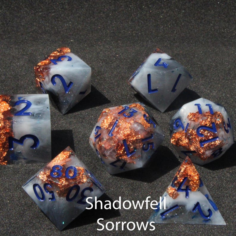 Beautiful blue, black and white resin dice sit on a black felt table top. Light shines down on the dice making the colours swirl into a maelstrom of epic colour. The dice include multicoloured foils that sparkle, shimmer and dance in the light.