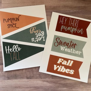 May include: Two printable signs with autumn-themed text. The first sign has the text "Let's get cosy", "Hello Autumn", and "Pumpkin Spice". The second sign has the text "Hey there pumpkin", "Sweater Weather", and "Autumn Vibes".