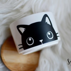 May include: White ceramic planter with a black cat face design. The cat's face is a simple, graphic illustration with large eyes, a nose, and whiskers. The planter sits on a wooden coaster. The Silvi Create logo is in the bottom right corner.