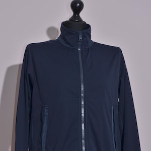 May include: A navy blue zip-up jacket with a high collar and two front pockets. The jacket is displayed on a mannequin. The jacket has a ribbed hem and cuffs. The zipper runs down the centre of the jacket.