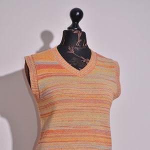 Può includere: Un gilet di maglia senza maniche con scollo a V e strisce orizzontali in tonalità di arancione, giallo e beige.