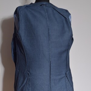Puede incluir: Un blazer azul oscuro exhibido en un maniqu&iacute;. El blazer tiene un dise&ntilde;o cl&aacute;sico con solapa de muesca y cierre de dos botones. La tela parece ser un tejido texturizado. La parte trasera del blazer es visible, mostrando las costuras y una abertura en la parte inferior.