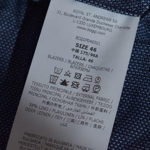 Puede incluir: Primer plano de una etiqueta de ropa blanca con texto negro, incluyendo la talla 46. La etiqueta est&aacute; adherida a una tela azul marino texturizada. La etiqueta tambi&eacute;n incluye instrucciones de lavado y la composici&oacute;n de la tela.