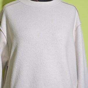 May include: A white, long-sleeved sweatshirt with a crew neck and a slightly cropped hem.