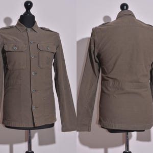 May include: A brown utility jacket with a button-up front, two flap pockets on the chest, and a belt at the waist.