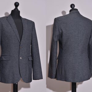 May include: A dark gray blazer with a textured fabric. The blazer has a two-button closure and two flap pockets.