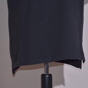 May include: A black t-shirt displayed on a mannequin. The shirt is a solid color and appears to be made of a soft material. The hemline is slightly uneven, adding a unique detail to the garment.