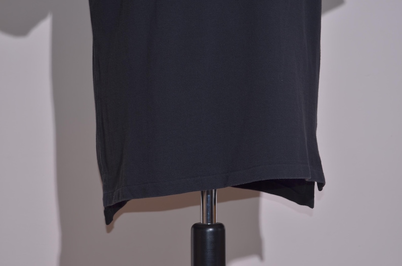 May include: A black t-shirt displayed on a mannequin. The shirt is a solid color and appears to be made of a soft material. The hemline is slightly uneven, adding a unique detail to the garment.