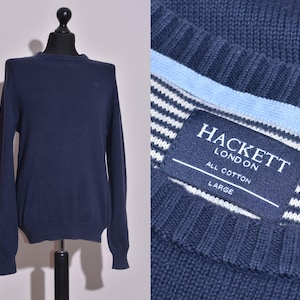 Puede incluir: Un suéter azul marino de manga larga con cuello redondo. El suéter tiene una banda blanca y azul a rayas alrededor de la parte inferior y una etiqueta que dice "Hackett London All Cotton Large".