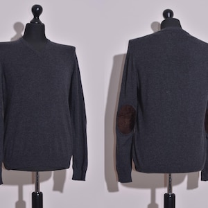 Puede incluir: Un suéter gris oscuro de manga larga con cuello en V y parches de cuero marrón en los codos.