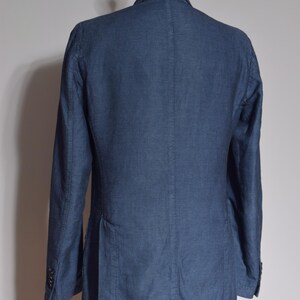 Puede incluir: Una blazer azul marino con cierre de dos botones, bolsillos visibles y solapas con muescas. La chaqueta se exhibe en un maniqu&iacute; negro. La tela tiene un patr&oacute;n sutil.