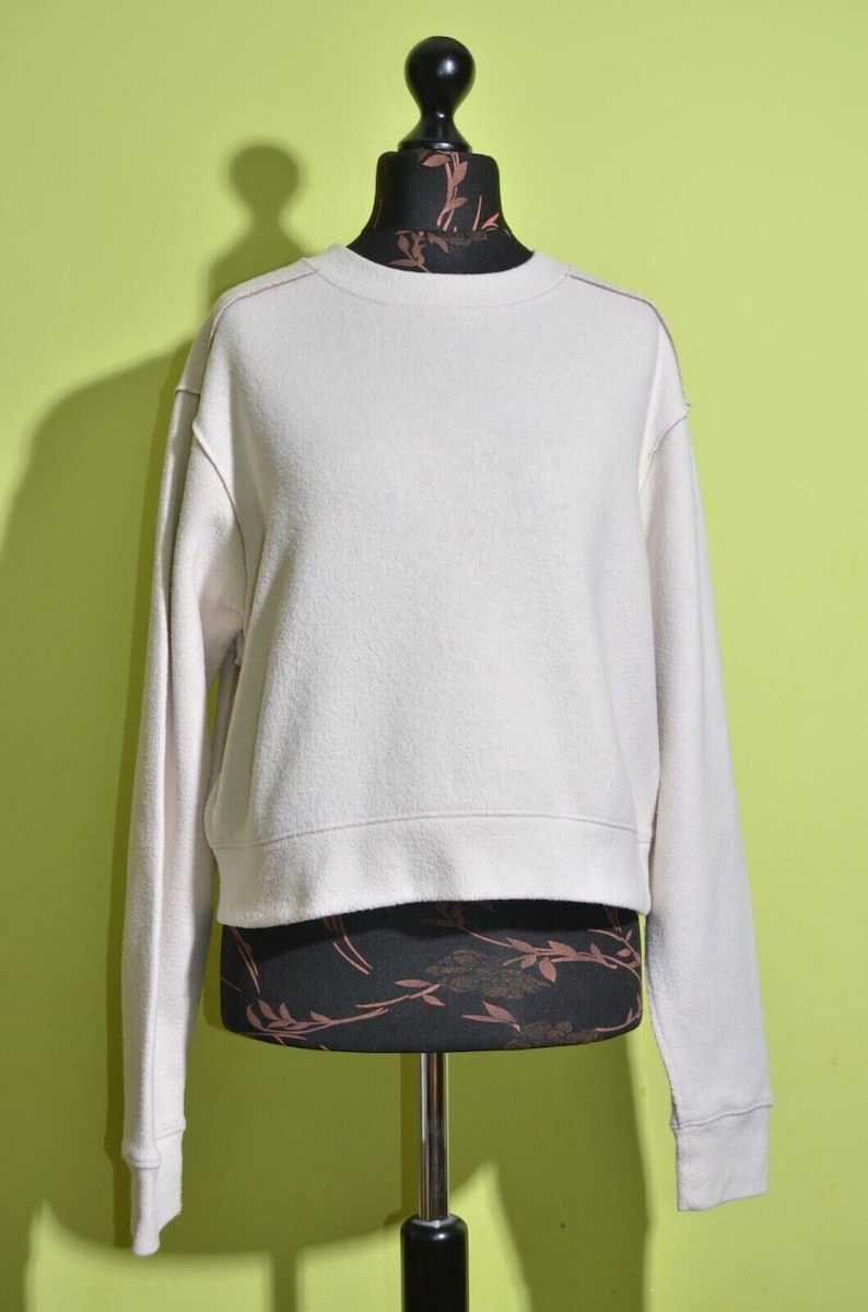 May include: A cream-colored cropped sweatshirt with long sleeves and a crew neck.