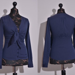 May include: A navy blue long-sleeved blouse with a tie at the neckline. The blouse has a button closure and a fitted silhouette.