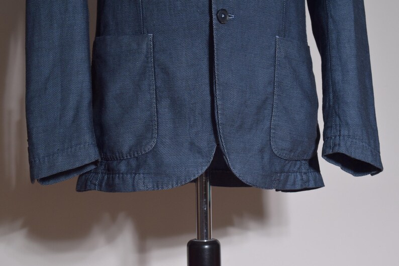 Puede incluir: Chaqueta azul marino con dos bolsillos delanteros y cierre de un solo bot&oacute;n. La chaqueta tiene una tela texturizada y un dise&ntilde;o cl&aacute;sico, adecuada para diversas ocasiones. Las mangas son largas.
