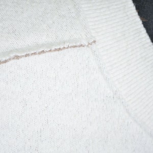 May include: Close-up of a white knitted sweater with a brown trim around the neckline.