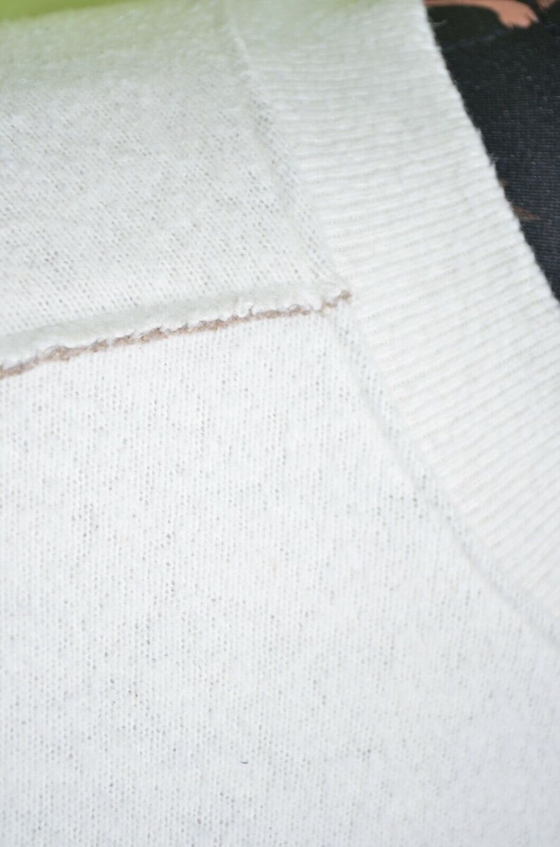 May include: Close-up of a white knitted sweater with a brown trim around the neckline.